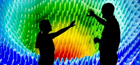 Computer scientists in silhouette stand before a vibrantly-colored computer visualization display. 