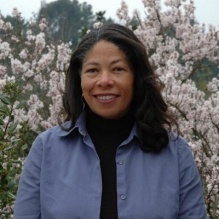 Portrait of Sheila Davis wearing a blue jacket and standing in front of flowers. 