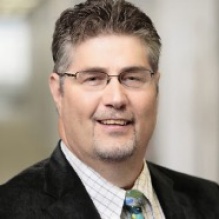 Portrait of Dennis Elsenbeck wearing a suit and tie. 