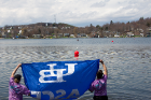 Two students members of ASCE's concrete canoe team hold up a blue and white "UB ASCE" flag facing a lake. 