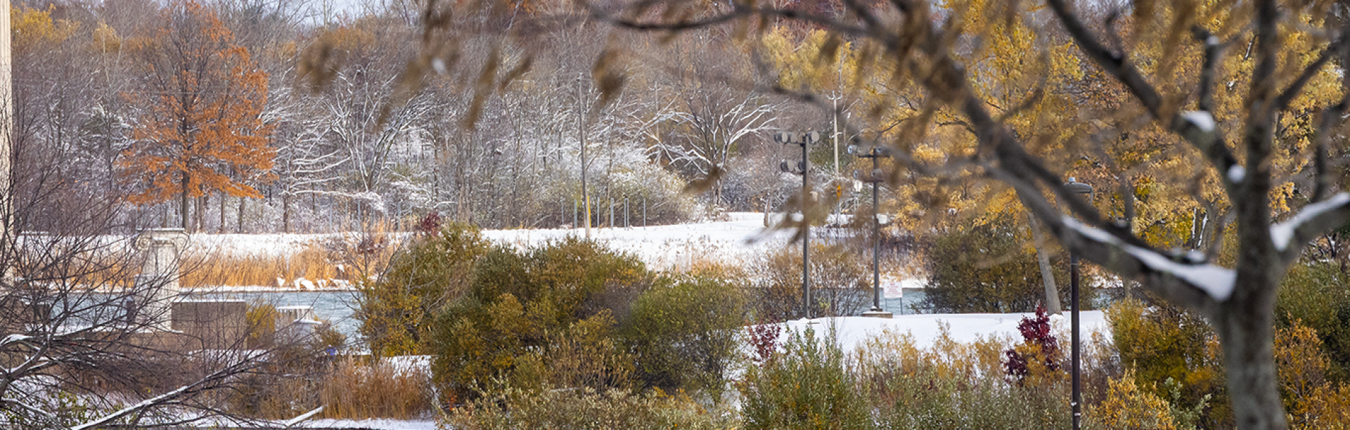 Three students walk along a a sidewalk covered with snow on either side. two of them are smiling, and the back of the other is facing the view+-.