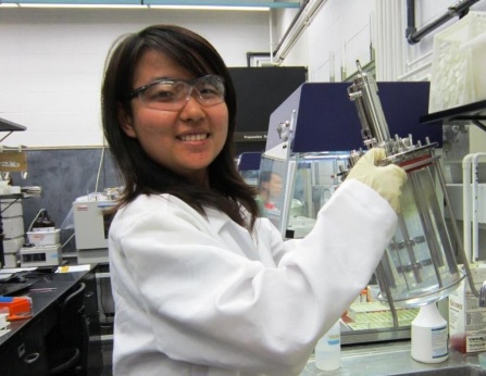 Student in lab coat comparing fluid in 2 vials. 