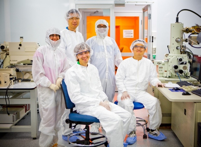 Five individuals wearing gowns, gloves, hairnets and shoe covers in the brightly lit UB Cleanroom. 