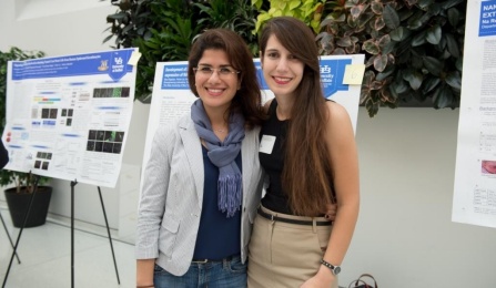 2 students posing front of their research posters at symposium. 