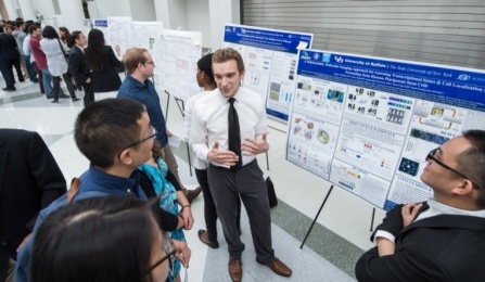 Student presenting poster to two students at graduate symposium. 