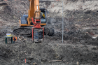 Excavator operating a hydraulic attachment in a muddy construction site excavation.