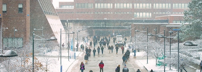 UB students walk along the UB academic spine as snow falls. 