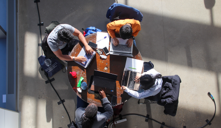 An aerial view of four students sitting on a table working on laptops. 