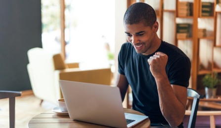 A student is smiling as he looks at a laptop. 