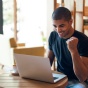A student is smiling as he looks at a laptop. 