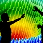 Computer scientists in silhouette stand before a vibrantly-colored computer visualization display. 