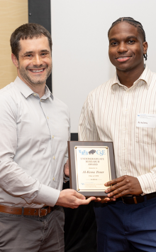 Al-Kesna Foster, 2024 recipient of the CSE Undergraduate Research Award stands smiling and holding his plaque with associate professor Luke Ziarek. 