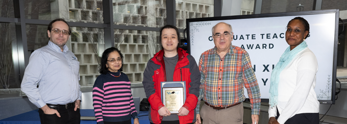 Oliver Kennedy, Bina Ramamurthy, the student recipient, Ken Regan, and Ifeoma Nwogu stand together smiling at the camera in the first floor of Davis Hall. 