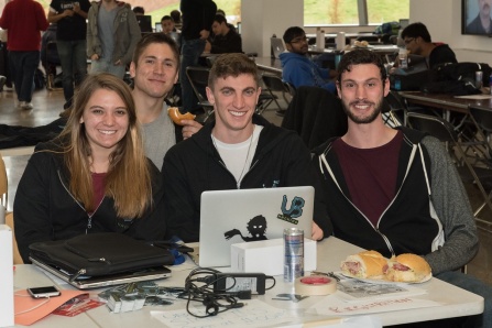 A group of four students are gathered together around a laptop screen. 