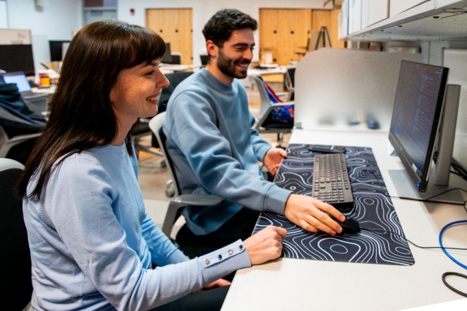 A CSE student and a professor smile as the student works at a desktop computer in a CSE lab.