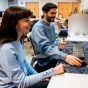 A CSE student and a professor smile as the student works at a desktop computer in a CSE lab. 