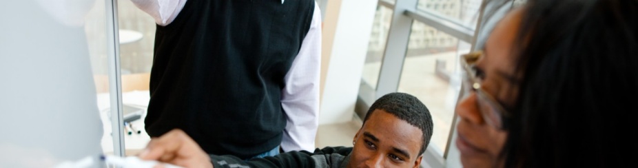 Assistant professor overlooks students writing on a white board. 