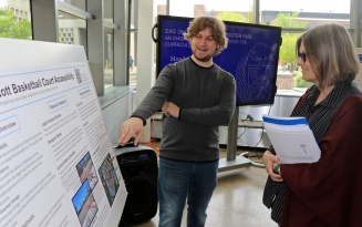 Student points to his poster and talks to a faculty member. 