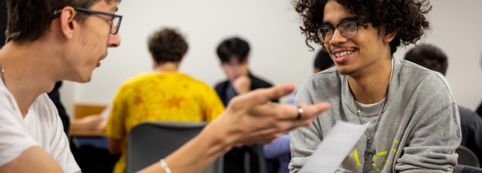 Two students converse in a classroom setting. 