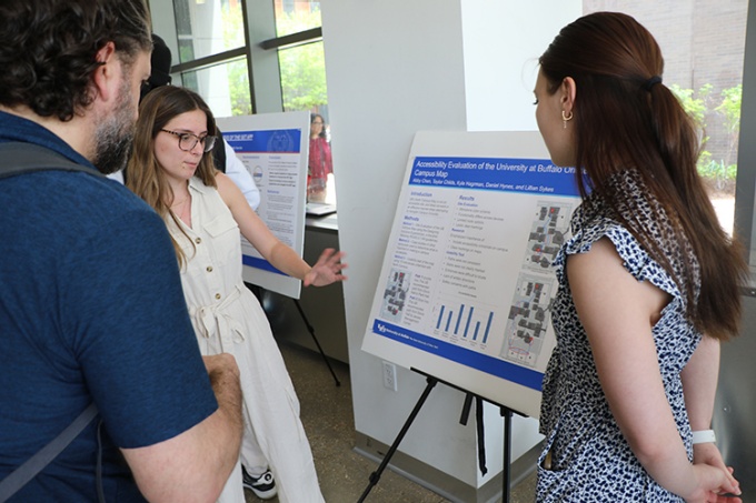 A student presents her research poster to faculty members. 