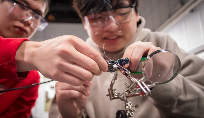 Students wearing safety glass practice a soldering technique. 