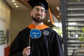 Person in cap and gown holding sign. 