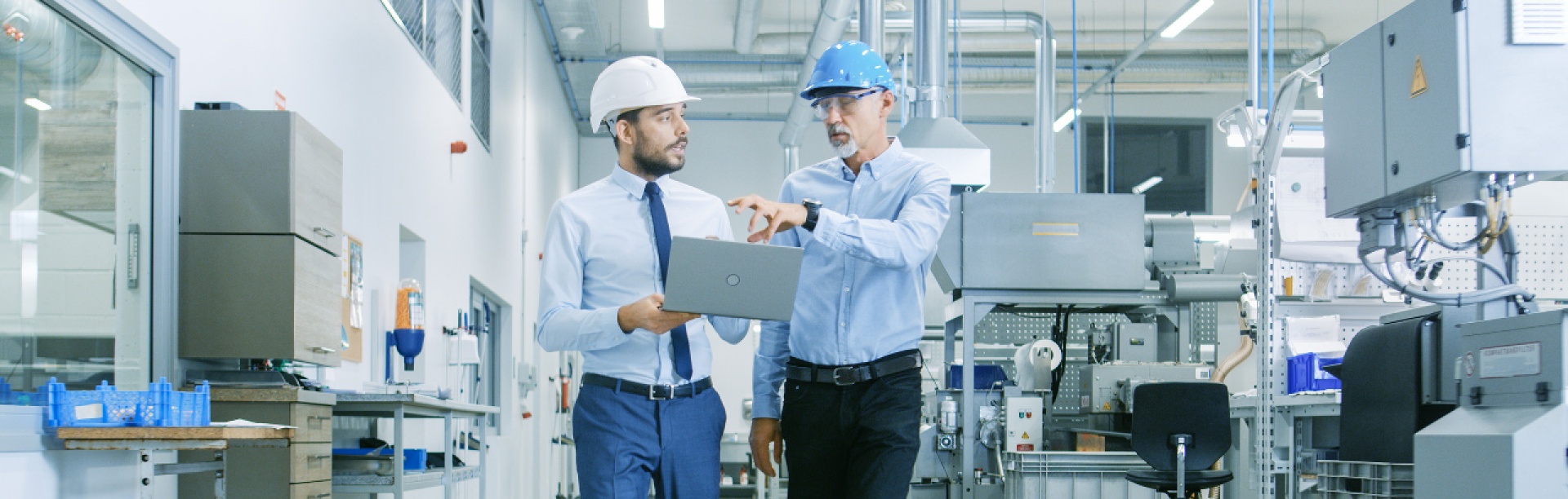 Two project managers in hard hats having a discussion, one holding a laptop. 