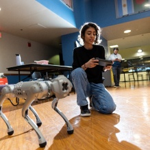 Student kneels next to robot dog. 