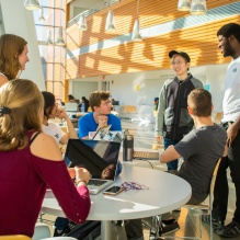 A student presenting as female discusses her research poster while holding a 3-D printed model of her research in one hand. 