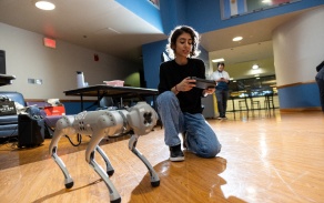 Student kneels next to robot dog. 