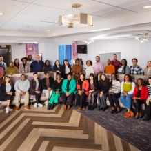 A student presenting as female discusses her research poster while holding a 3-D printed model of her research in one hand.