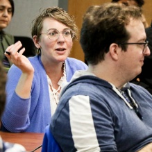 A student presenting as female discusses her research poster while holding a 3-D printed model of her research in one hand.