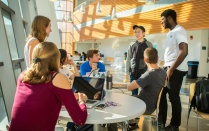 A student presenting as female discusses her research poster while holding a 3-D printed model of her research in one hand. 