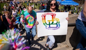 A person holding a poster with a UB logo in rainbow colors. 