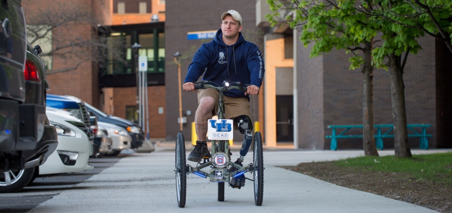 Man with prosthetic leg riding a tricycle outside Jarvis Hall. 