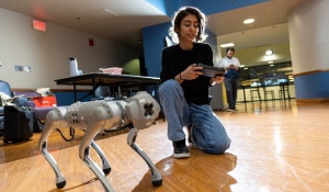 Student kneels next to robot dog. 