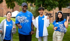 Students standing in a group, wearing blue and smiling. 