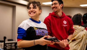 Engineerinng Week, Bot Wars in the Student Union, students smiling while one holds a controller.