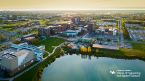 Background 7: Drone view of University at Buffalo North Campus academic buildings and Lake LaSalle at sunset with the School of Engineering and Applied Sciences logo in the bottom right corner. 