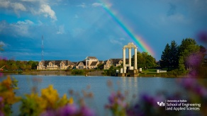 Background 5: Baird Point from accross Lake LaSalle with flowers in the foreground, a rainbow in the sky, and the School of Engineering and Applied Sciences logo in the bottom right corner. 