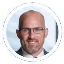 Profile picture of Kemper Lewis, a bald and bearded white man with glasses wearing a suit, in Davis Hall. 