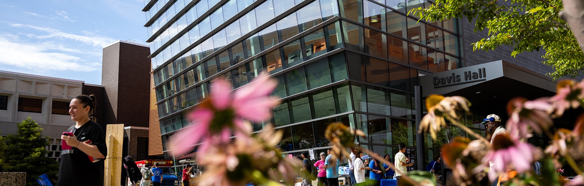 A spring day outside of UB's Davis Hall, as students mill about outside with blue skies overhead. 