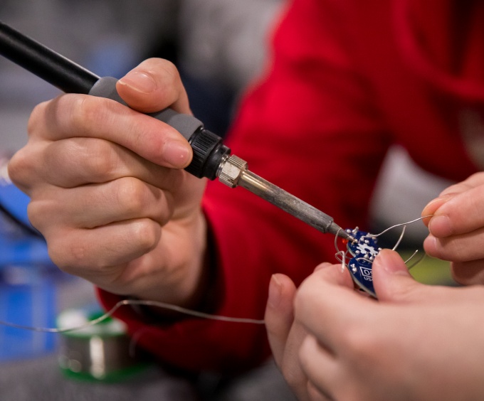 Two pairs of hands are sodering a mechanical device. 