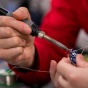 Two pairs of hands are sodering a mechanical device. 