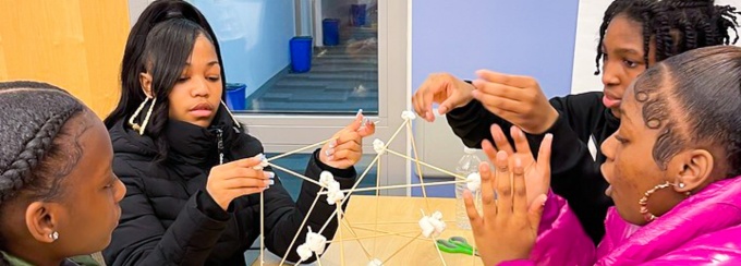Four female grade-school students build a structure using marshmallows and sticks. 