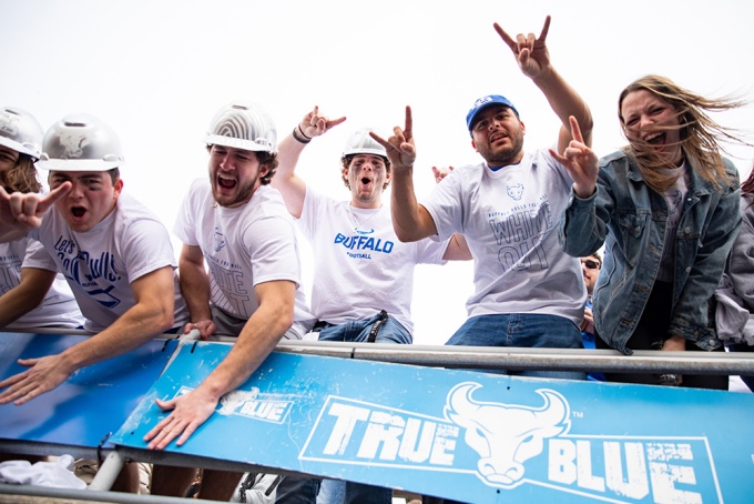 Group of students with UB horns up, cheering on the Bulls at a UB football game. 