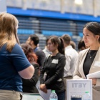 A student in professional attire speaking to a recruiter at a career fair. 