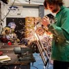 A man cutting a piece of metal with an electric saw, causing sparks to fly. 