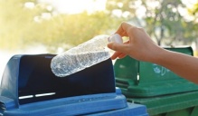 Hand throwing a plastic water bottle into a recycling bin. 