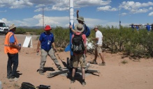 Five people in sun hats work to launch a small-scale rocket in the desert.